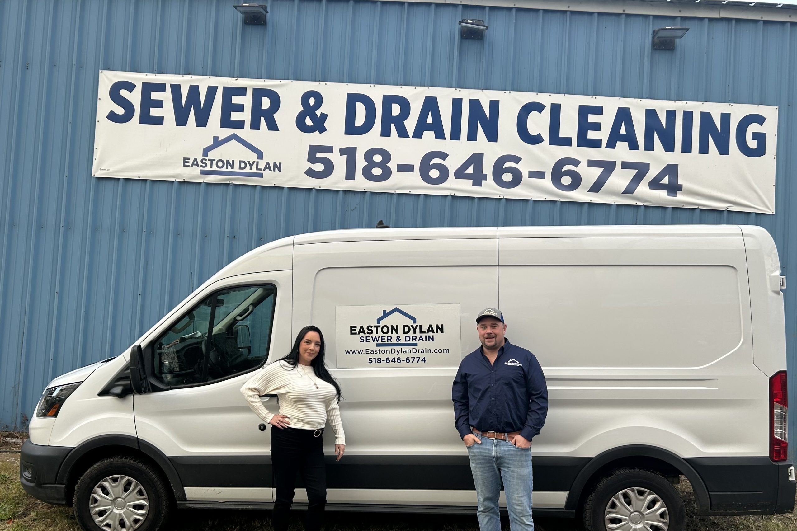 Owners of Easton Dylan Sewer & Drain posing with company van under a banner reading: Sewer and drain cleaning