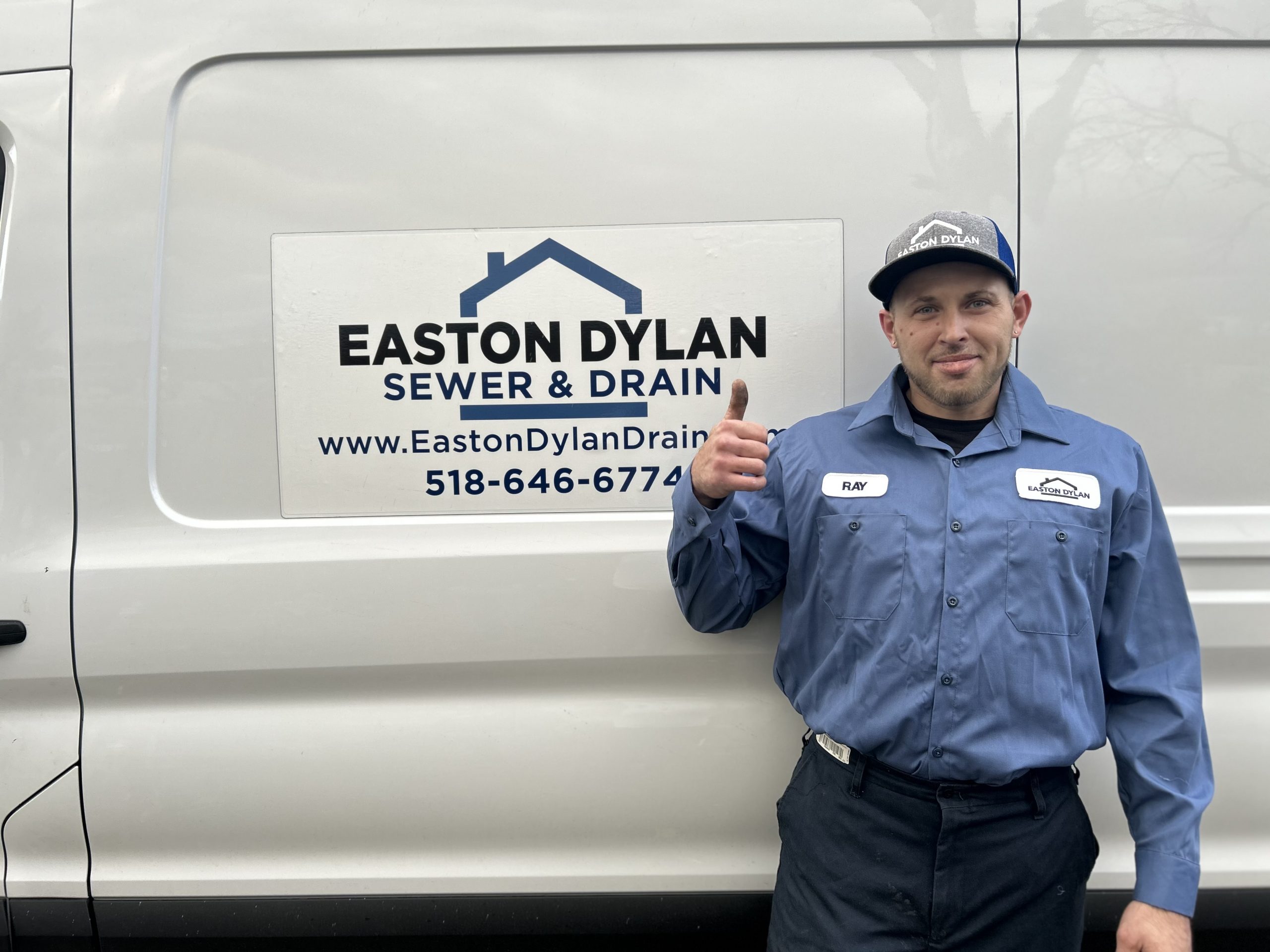 Plumber from Easton Dylan Sewer & Drain standing in front of the company's van, giving a thumbs-up